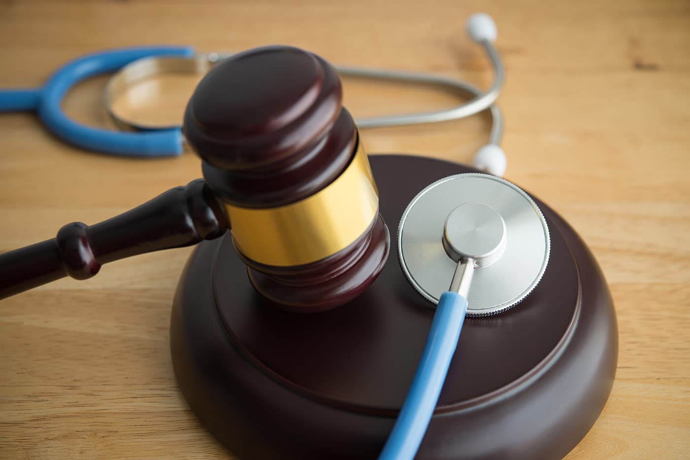 A wooden judge's gavel and a stethoscope resting together on a wooden surface, representing health care law and regulation.