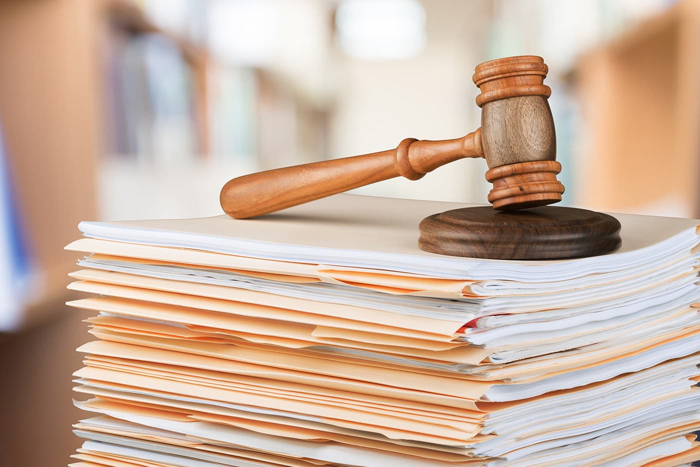 A wooden gavel resting on a large stack of manila file folders